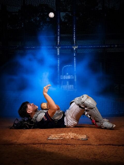 Catcher lying on the dirt by home plate with the ball in the air