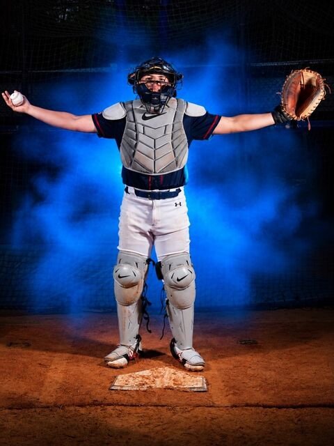 Catcher standing with arms open, ball in one hand and glove in the other