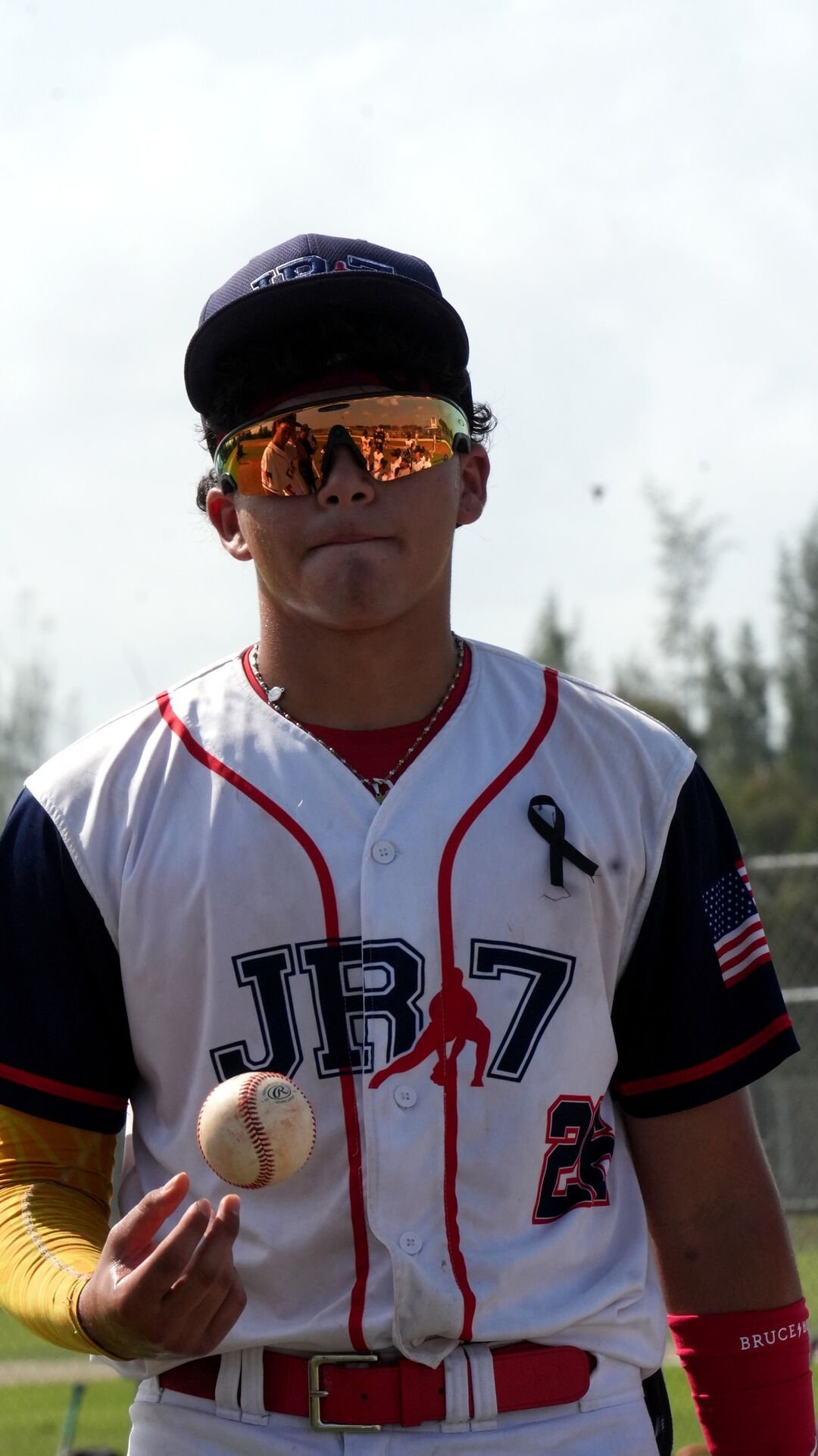 Baseball player in a white uniform and sunglasses holding the ball