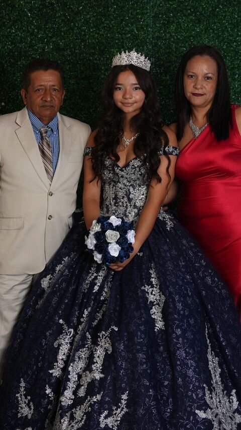 The quinceañera with two companions in front of the greenery wall