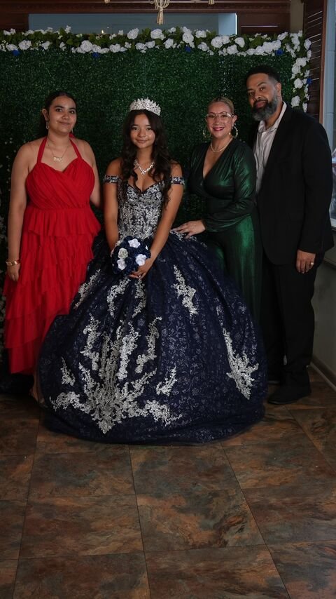 The quinceañera with companions in front of the greenery wall