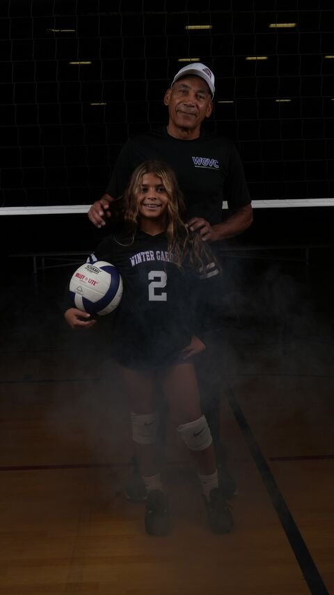 Coach and volleyball player posing with the ball on the court